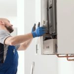 تکنسین با دستکش آبی در حال تعمیر پکیج دیواری سفید در خانه