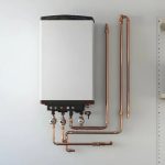 یک پکیج سفید رنگ که روی دیوار نصب شده با لوله‌های مسی براق